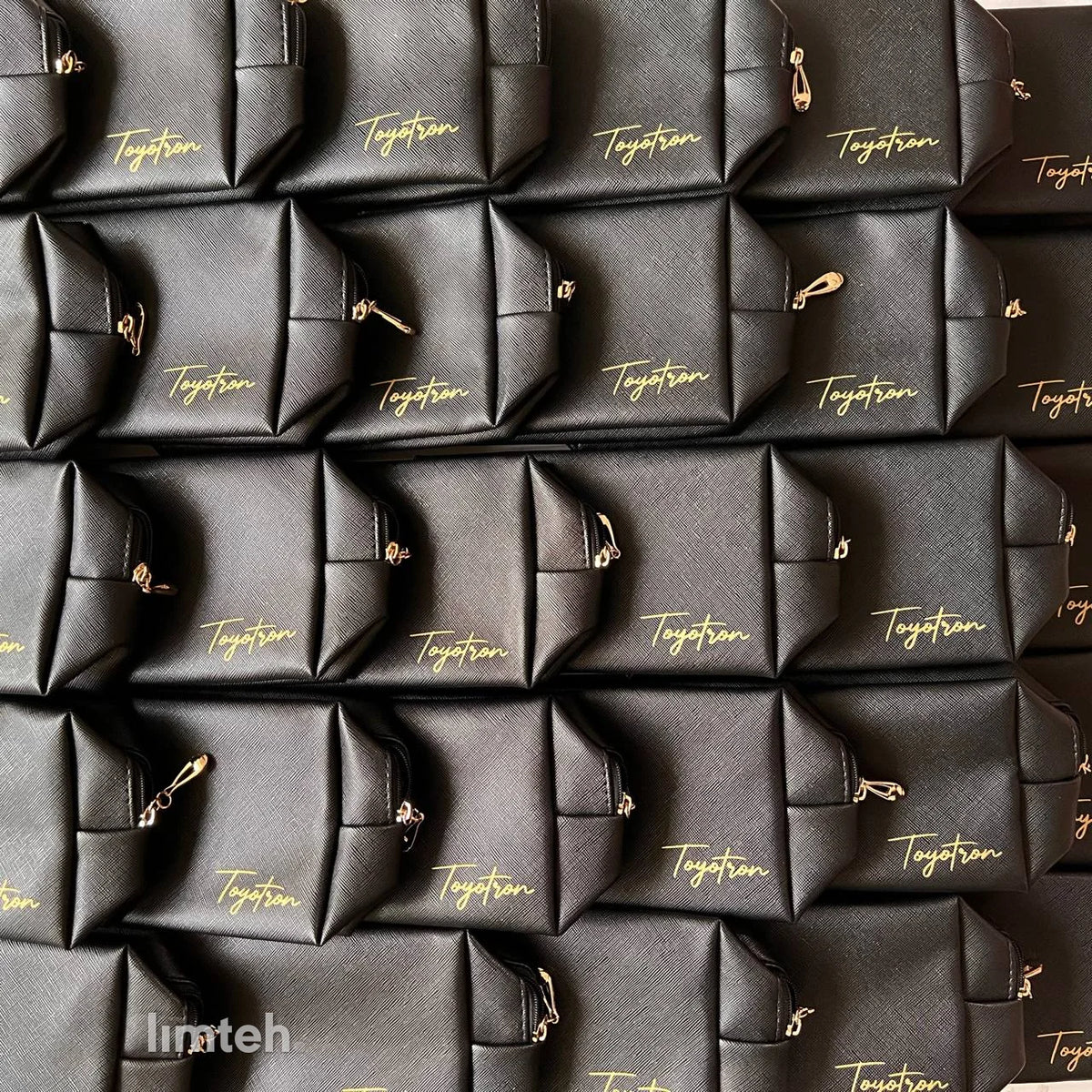 Black Saffiano-textured leather zip pouches with gold branding and gold zip pulls, arranged face-up in neat rows.