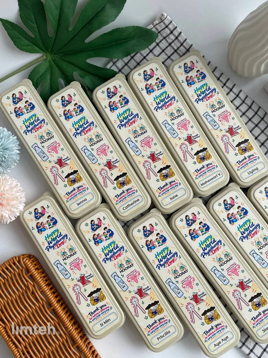 A set of wheat-straw cutlery cases printed with colourful 'Happy World Physiotherapy Day' artwork and individual names, arranged in rows on a light surface with faux foliage and flowers.