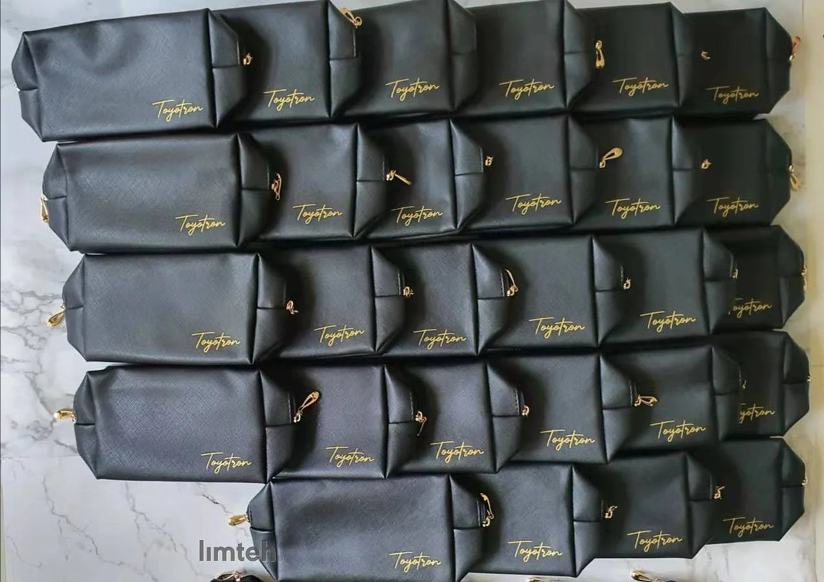 Black Saffiano-textured leather zip pouches with gold branding and gold zip pulls, arranged face-up in neat rows.