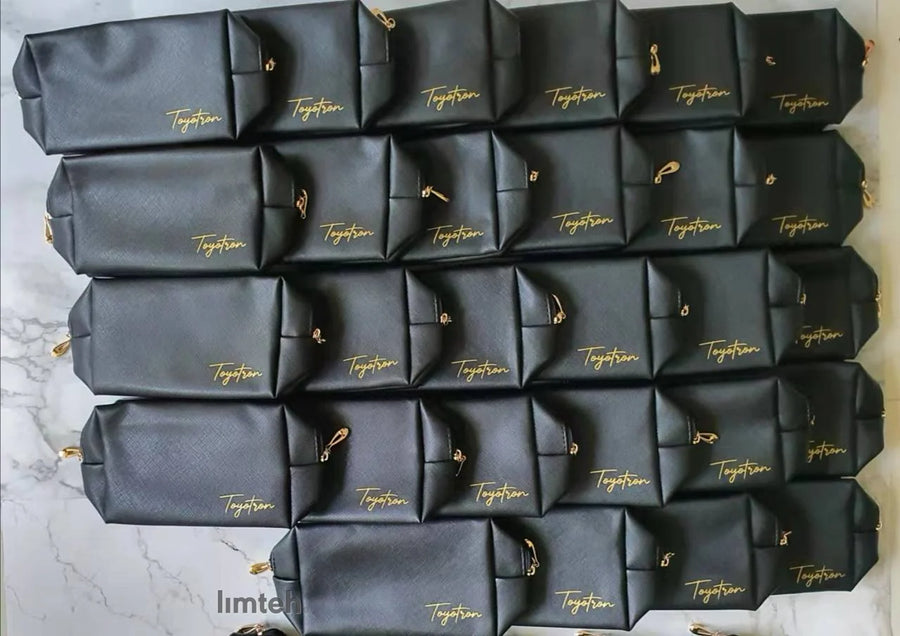 Black Saffiano-textured leather zip pouches with gold branding and gold zip pulls, arranged face-up in neat rows.