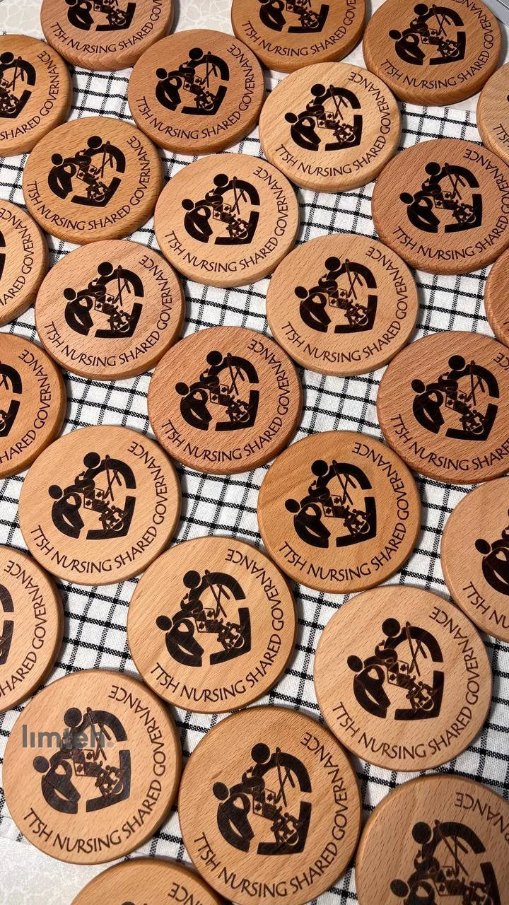 A spread of round beech-wood coasters, each laser-engraved with a circular organisation logo and curved text, arranged in overlapping rows on a black-and-white checked cloth.