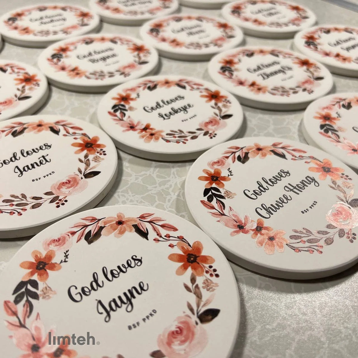 Round white diatomite coasters arranged in rows, each printed with a watercolour floral wreath around a personalised name.