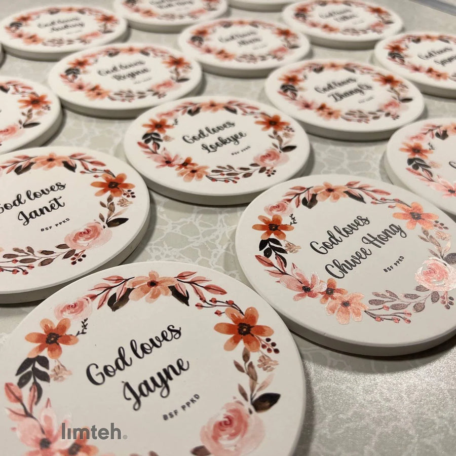 Round white diatomite coasters arranged in rows, each printed with a watercolour floral wreath around a personalised name.