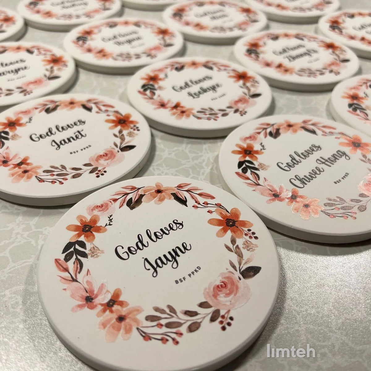 Round white diatomite coasters arranged in rows, each printed with a watercolour floral wreath around a personalised name.