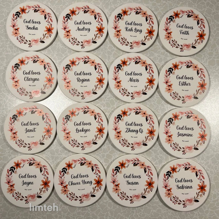 Round white diatomite coasters arranged in rows, each printed with a watercolour floral wreath around a personalised name.