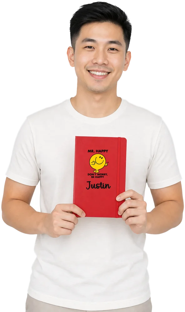 Man holding a Rose Red A5 notebook printed with the Mr. Happy graphic and the name Justin